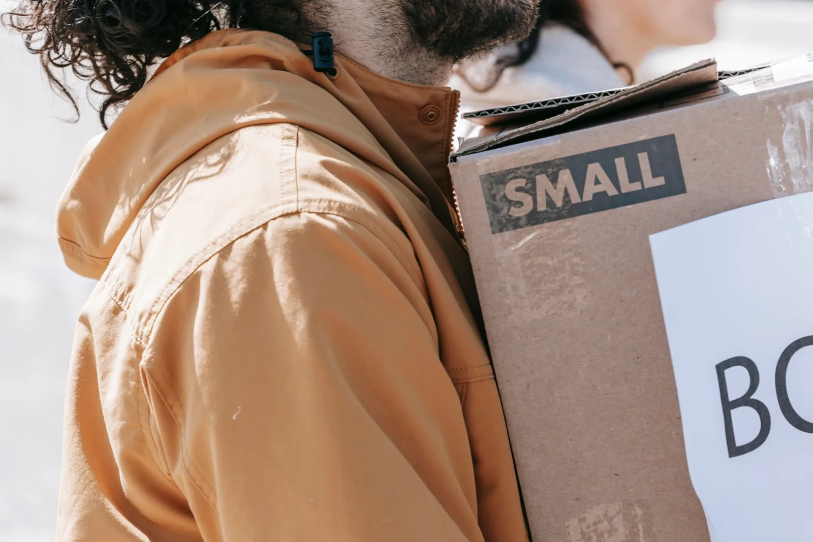 Two people carrying cardboard boxes outdoors in daylight while moving to a new home