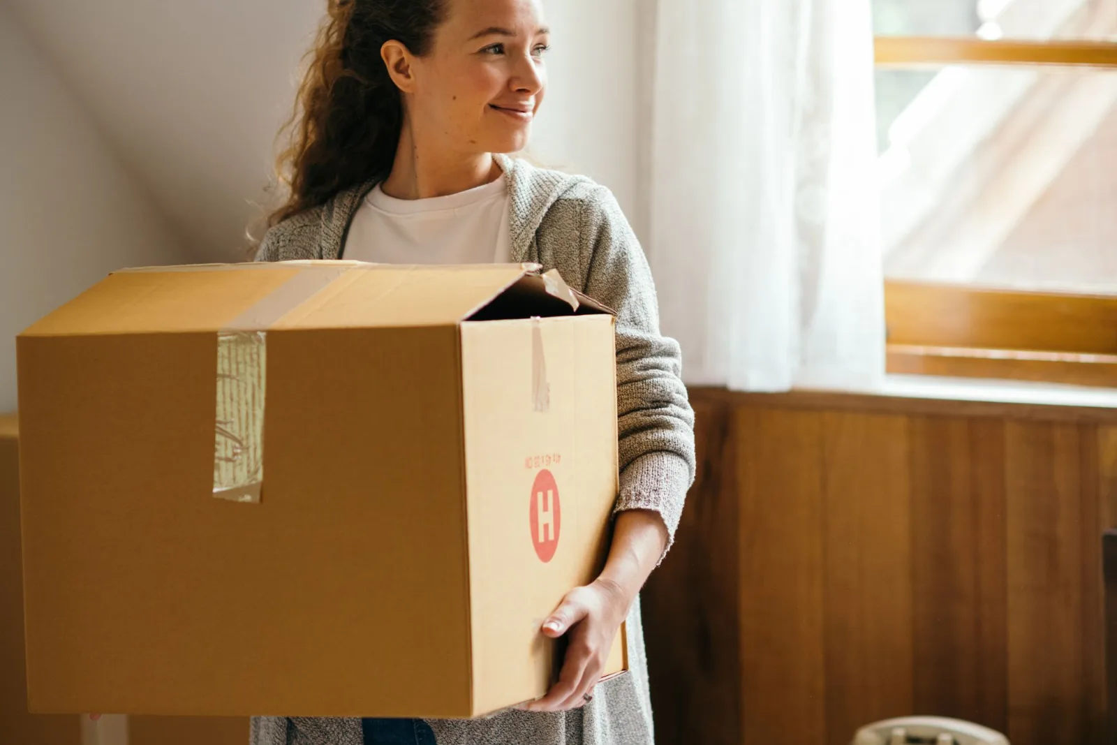 A person smiling while carrying a cardboard carton out of a house
