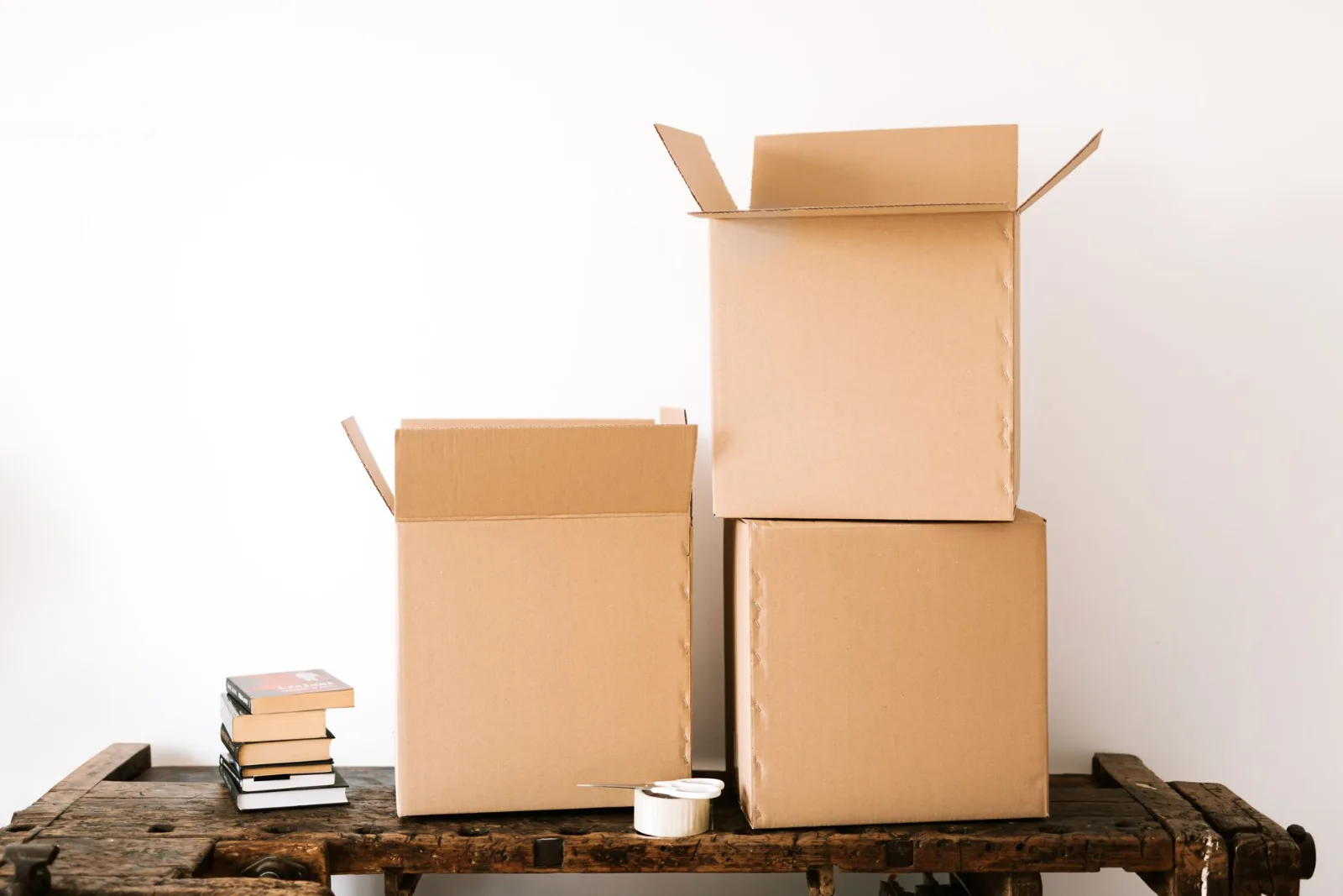 Opened cardboard cartons, a stack of books and a roll of tape on a wooden table