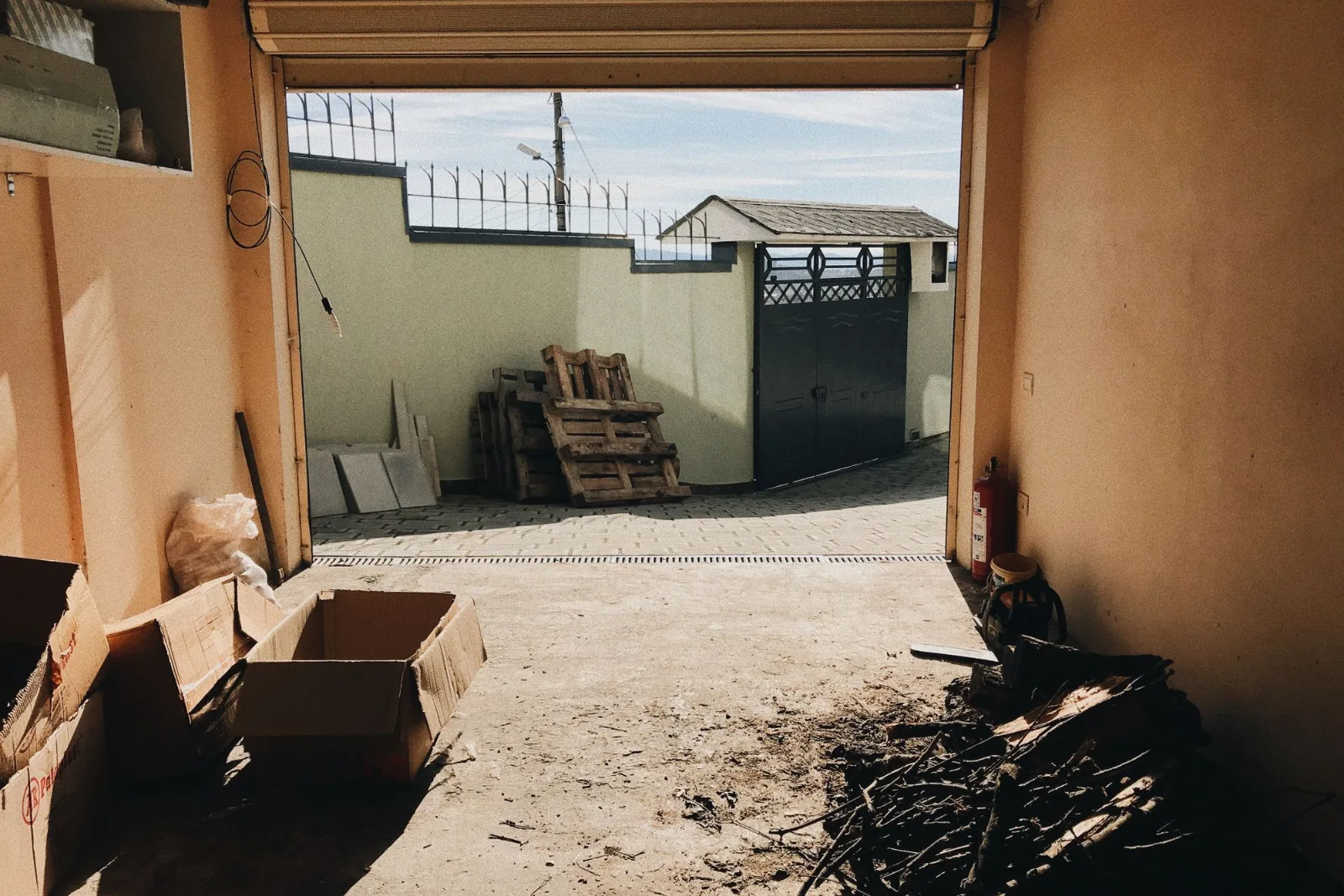 A view from inside a garage with the roller door open and cardboard boxes stacked inside