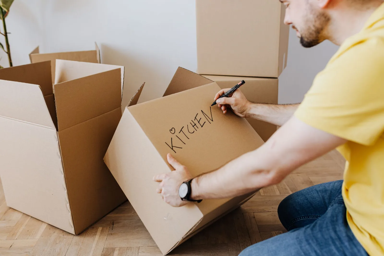 A person writing the word kitchen on a cardboard carton with a marker