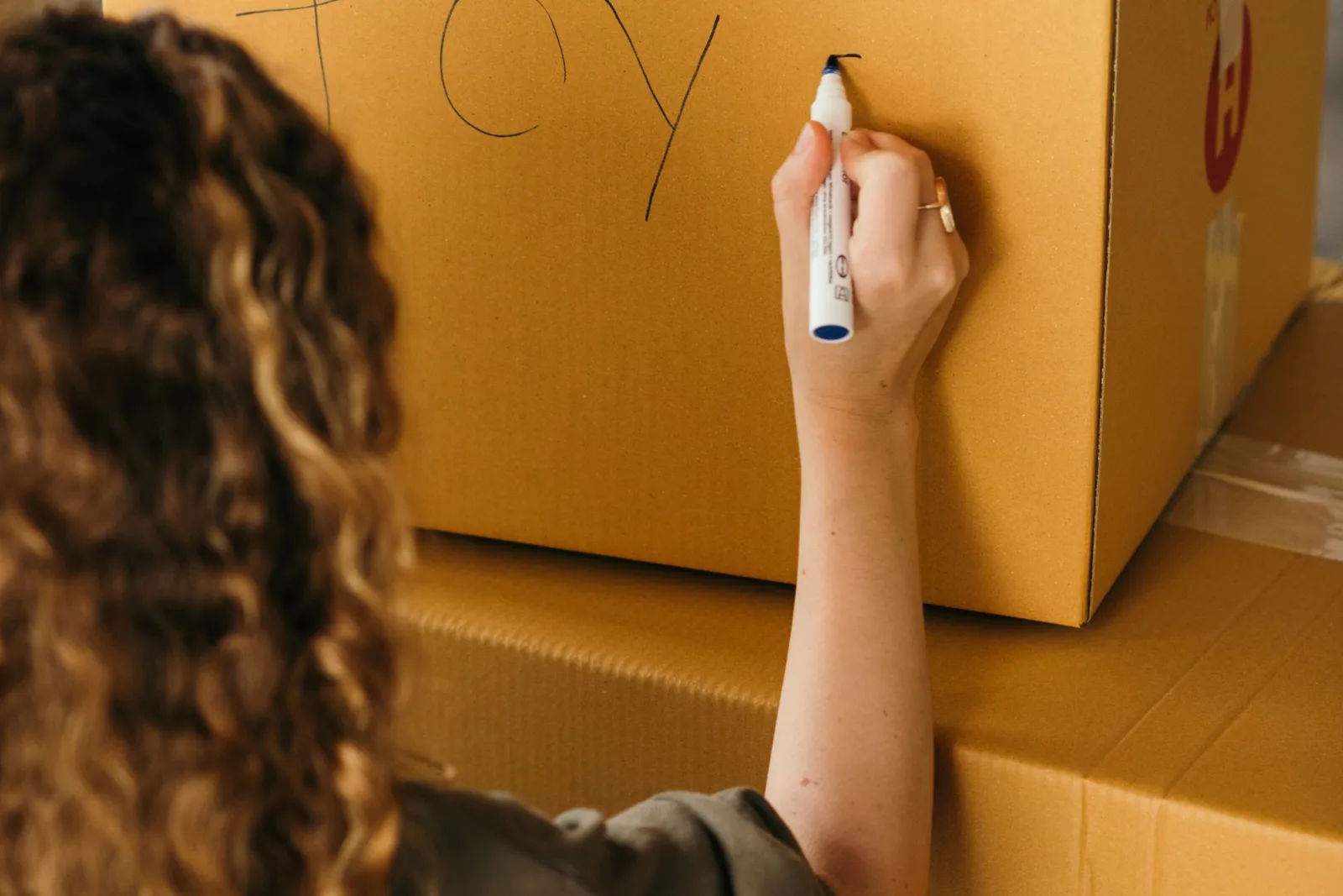 A person labelling a sealed cardboard carton with a marker pen
