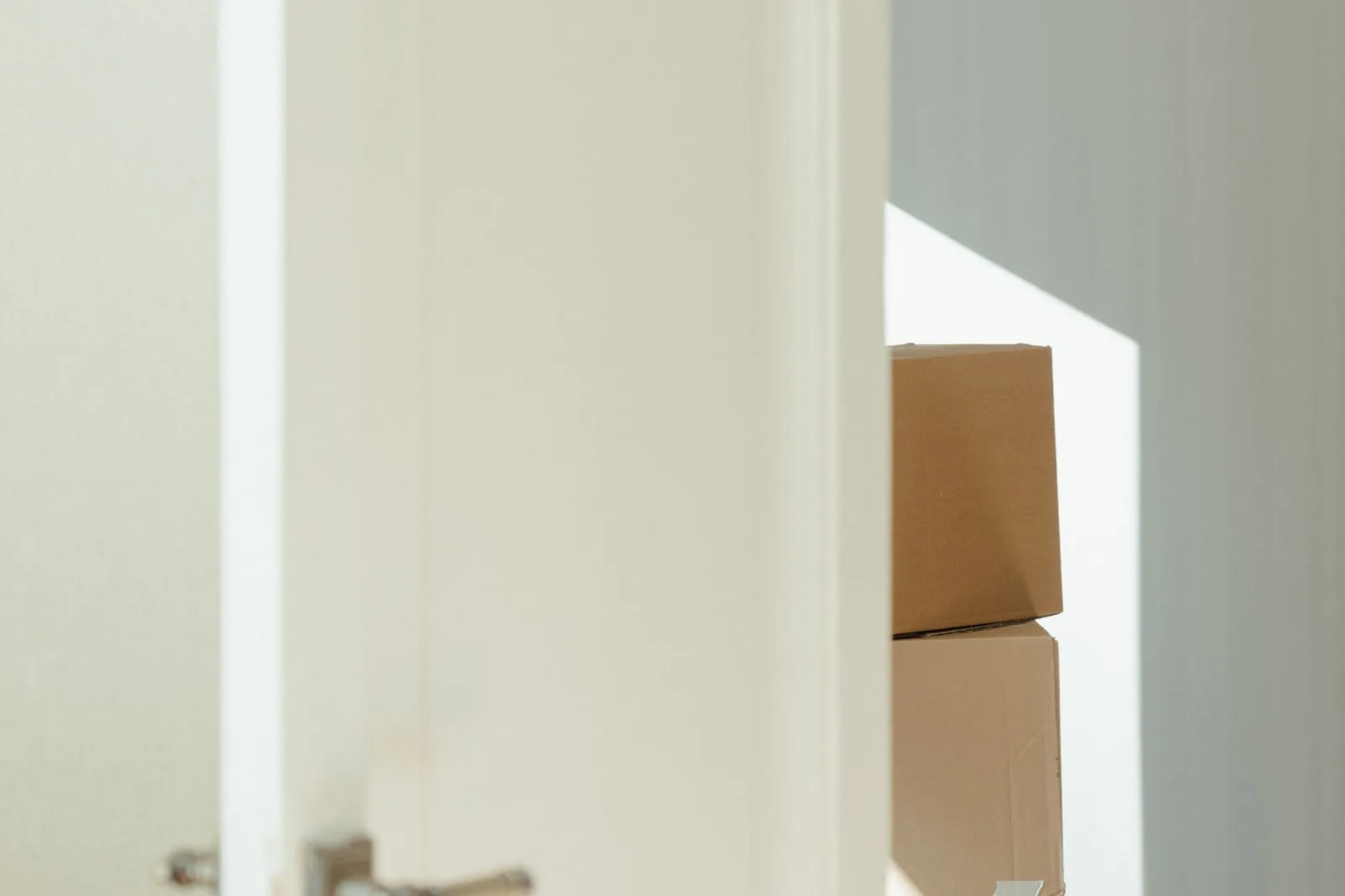 An open white door revealing stacked cardboard boxes in a bright interior