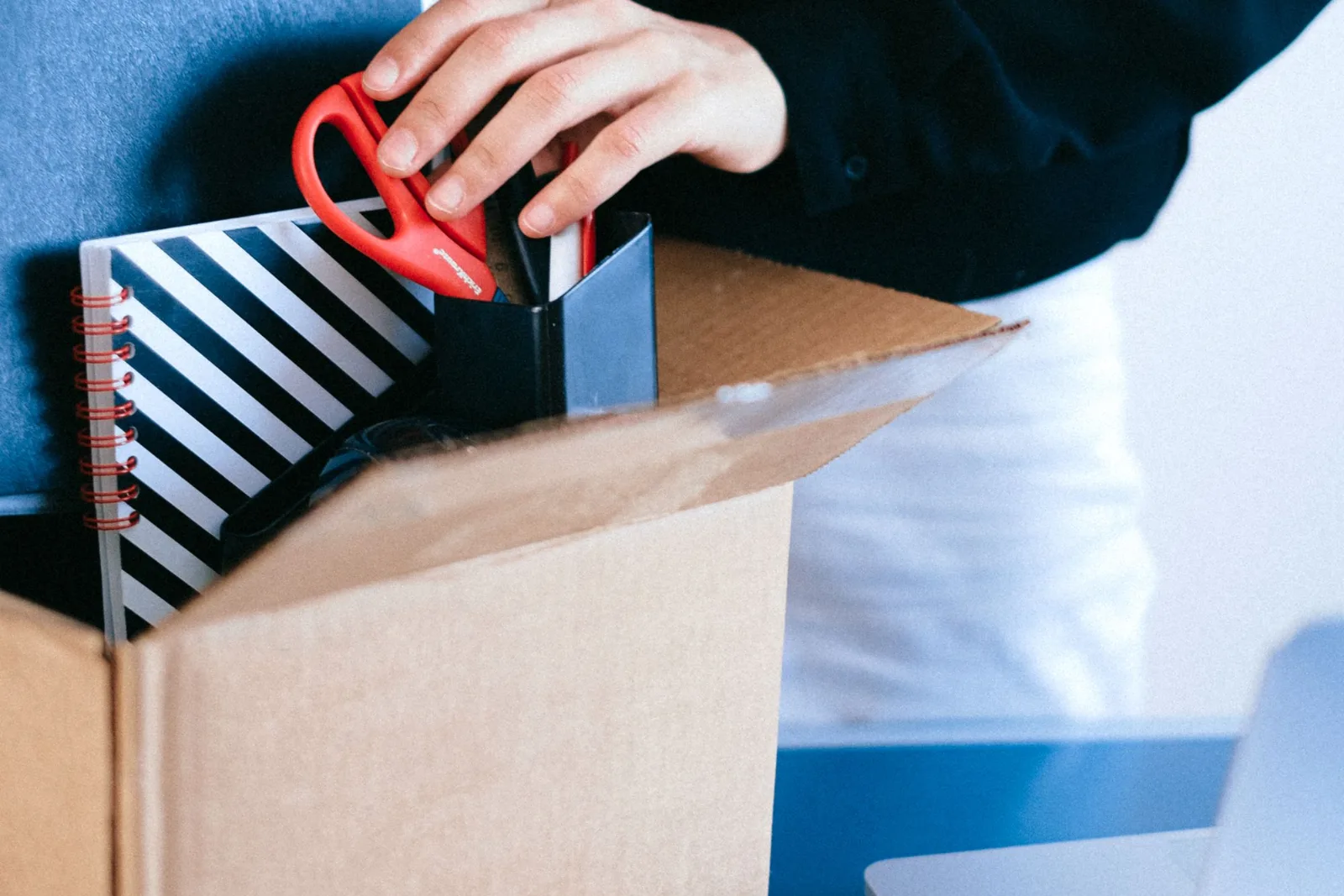 A person organising office supplies into a cardboard box at a desk
