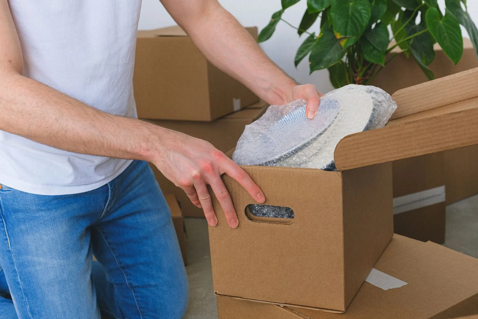 A person wrapping ceramic plates and stacking them into a cardboard carton before a move