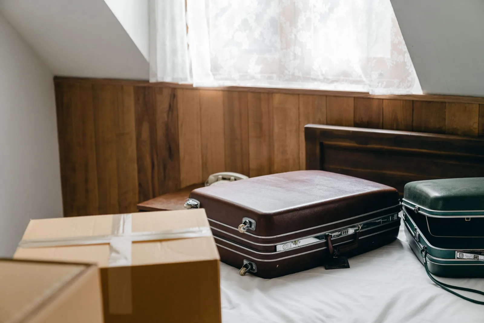 Vintage suitcases and packed cardboard cartons arranged on a bed