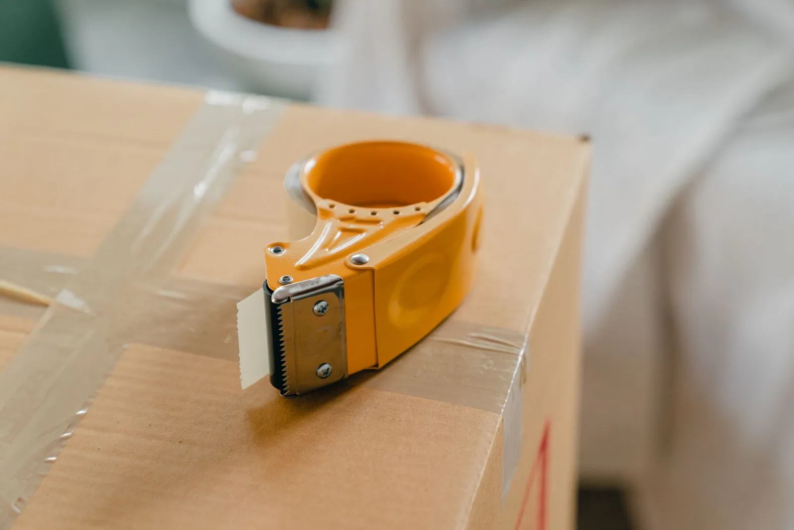 A yellow tape gun dispenser resting on a packed cardboard box