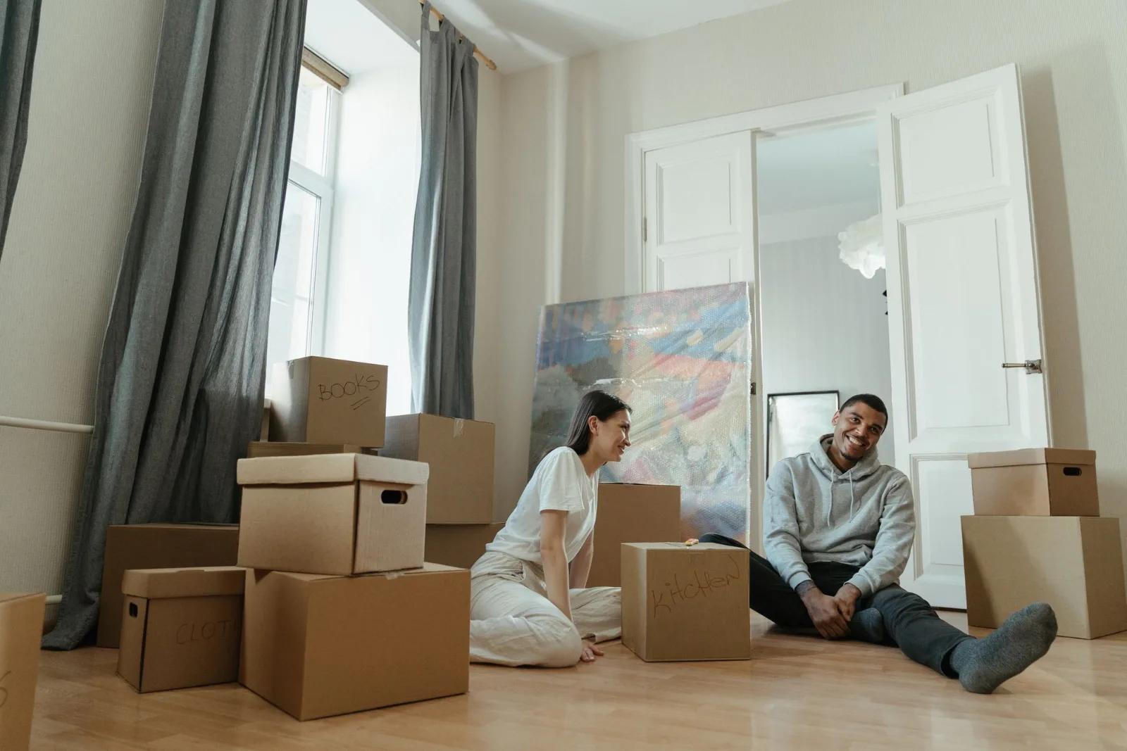 Two people surrounded by cardboard boxes while moving into a new apartment