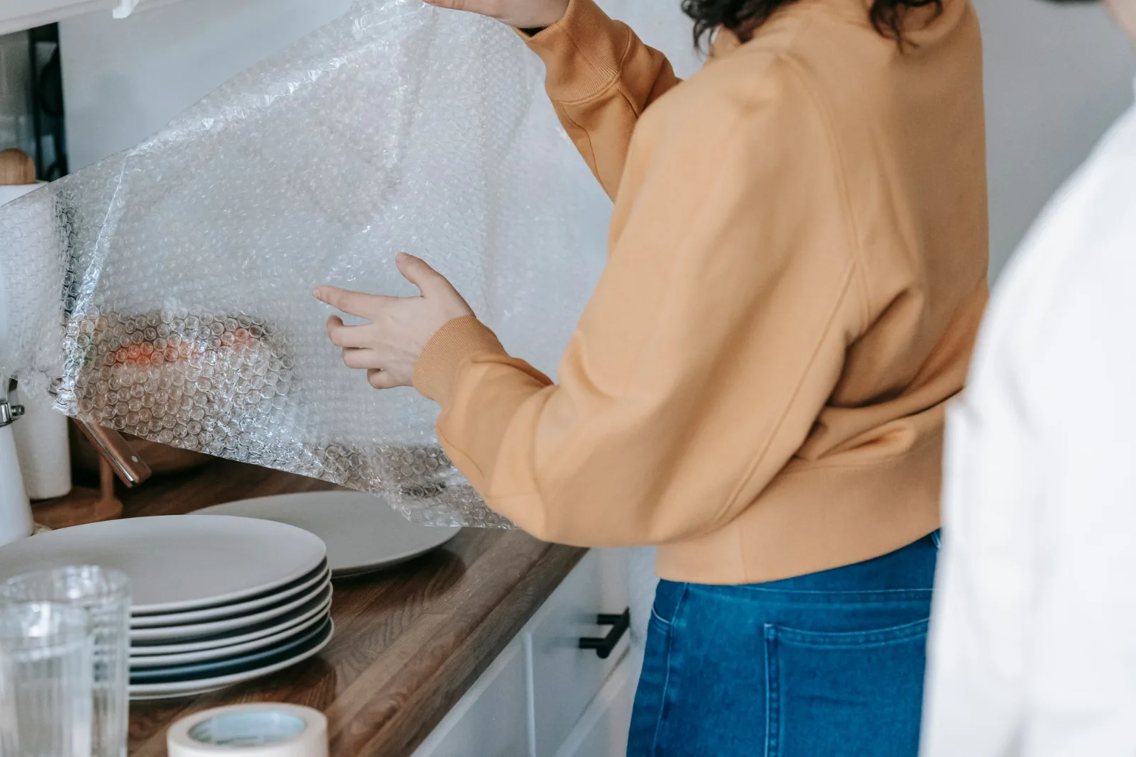 A woman carefully wrapping dishes in bubble wrap in a kitchen before a move