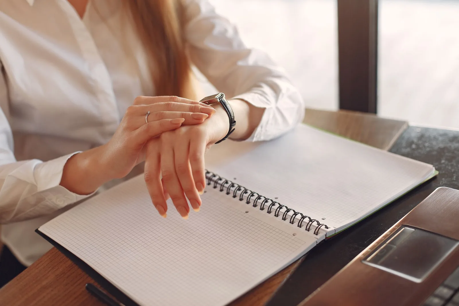 A person working at a wooden table beside a laptop and notes